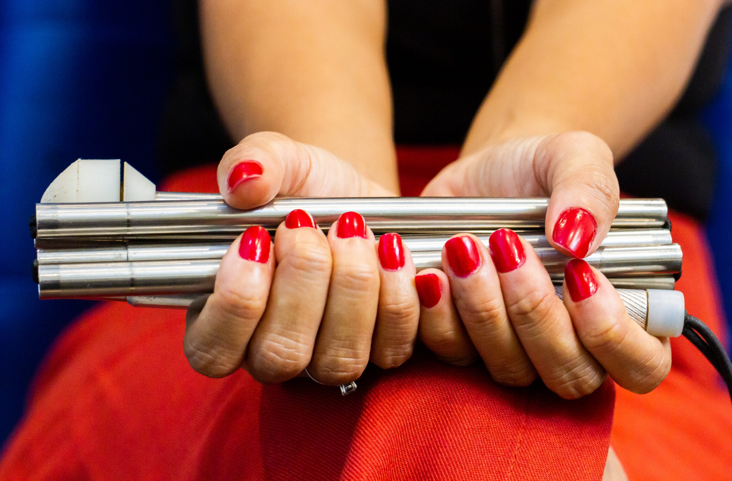 Mão de mulher negra segurando bengala com unhas vermelhas